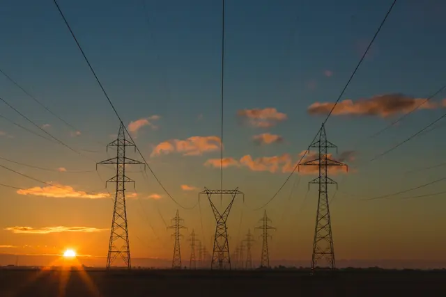 Steel lattice electricity transmission towers and power lines at sunset.
